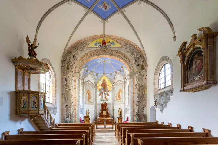 Innenraum der Hauskapelle St. Raphael mit bemaltem Chor und Holzbänken