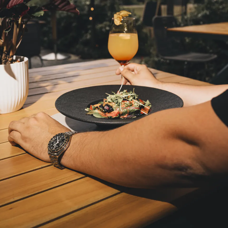 Gast mit Aperitif am Tisch, im Hintergrund das Piusheim
