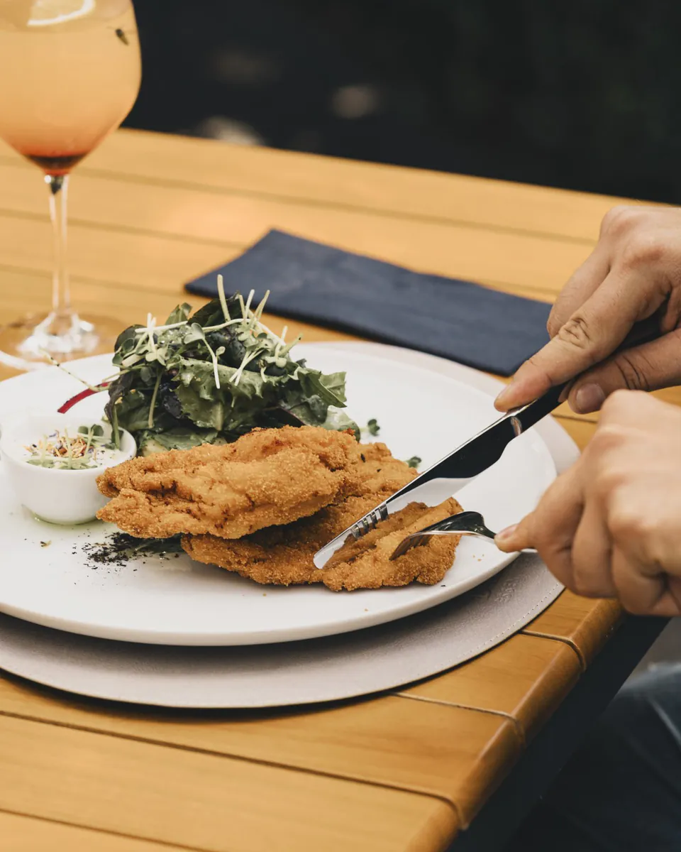 Gast schneidet ein Wiener Schnitzel mit Salat am Tisch